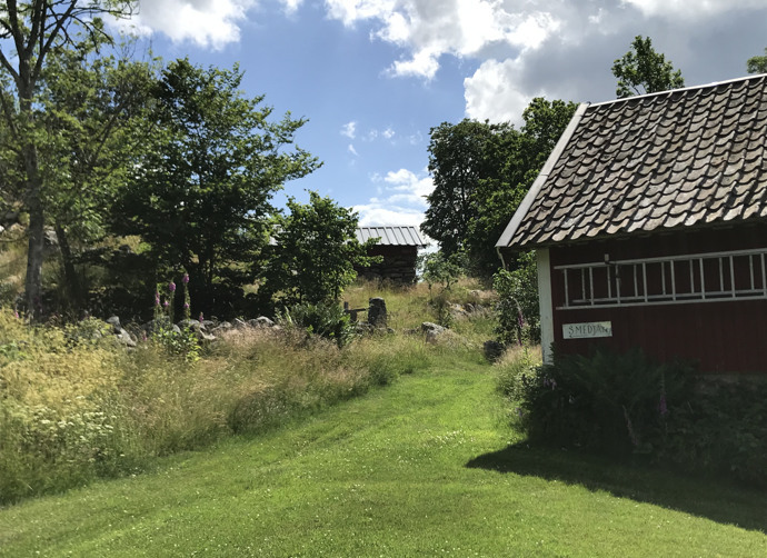 Ett rött hus med vita knutar omges av välklippt gräsmattan som gränsar till en frodig grön äng.