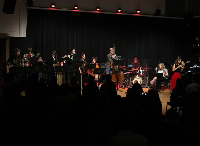 En grupp ungdomar spelar en konsert inför publik. Blåsinstrument, cello, kontrabas, trummor, gitarr, sång och keyboard. 