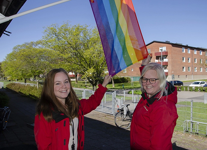 två pedagoger står och håller en prideflagga