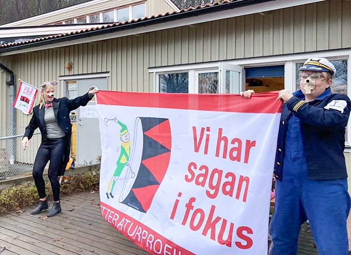 utklädda pedagoger står och håller upp flagga med texten vi har sagan i fokus