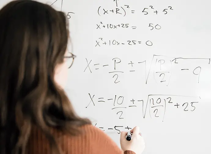 Elev skriver matematiska uträkningar på whiteboard under lektion.