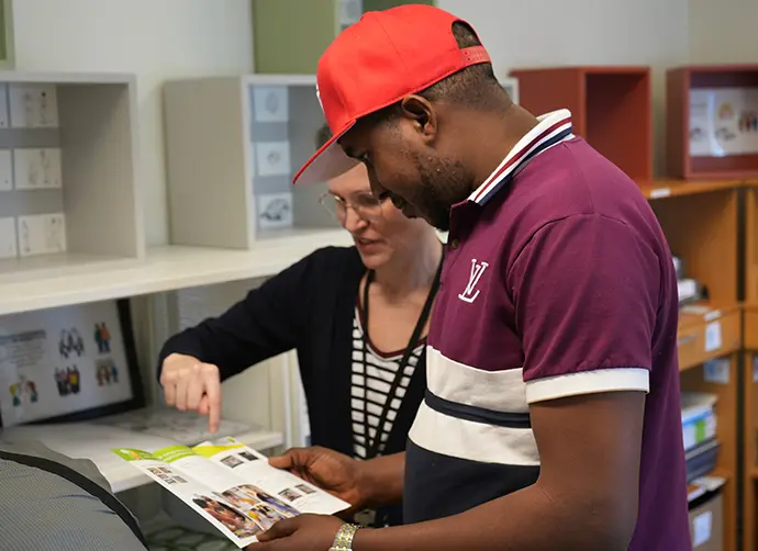 Två personer går igenom ett informationsblad tillsammans i ett rum med pedagogiskt material och hyllor i bakgrunden.
