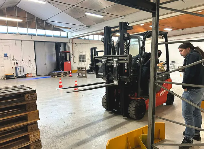 Person övar truckkörning inomhus i lagerlokal med pallar och koner.