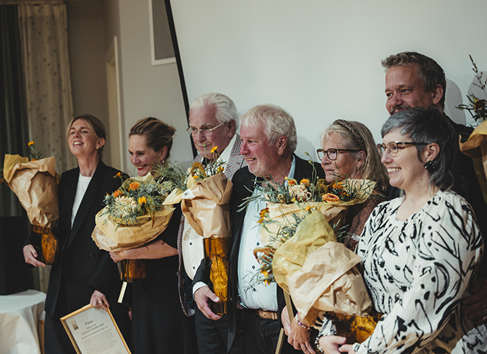 En samling finklädda människor står uppställda hållandes i blommor och diplom.