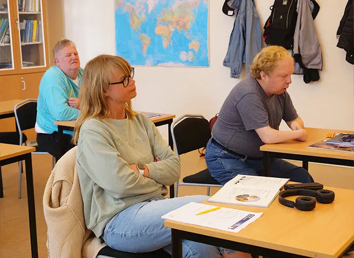 Tre elever sitter vid sina bänkar och lyssnar på en lektion.