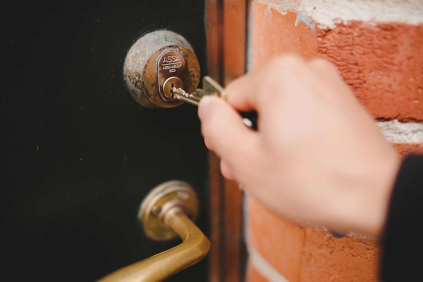 En hand håller i en nyckel som sätts i ett dörrlås till en bostad.