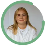 Emelie Hall har blont hår och bär en vit skjorta med smycken. Hon sitter framför en ljus bakgrund och ser glad ut.