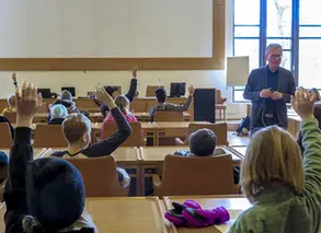 elever sitter och räcker upp händerna i koomunfullmäktigesalen