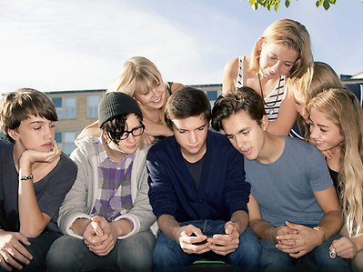Flera ungdomar tittar ned på en telefon.
