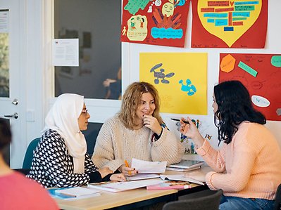 Tre kvinnor diskuterar i ett klassrum.